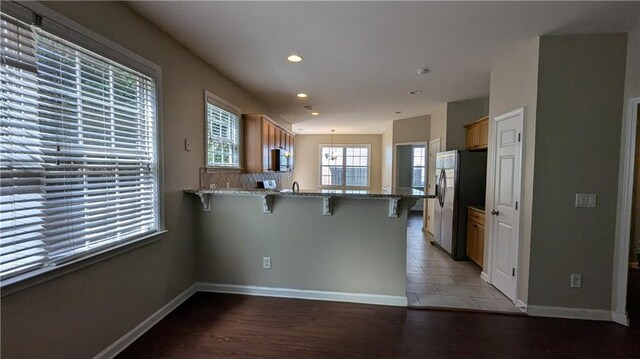 kitchen with tile patterned flooring, stainless steel fridge, kitchen peninsula, and a kitchen breakfast bar