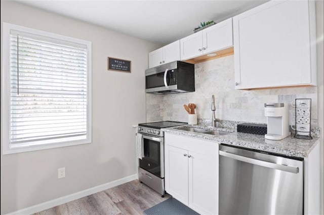 kitchen featuring light stone countertops, sink, white cabinetry, light hardwood / wood-style floors, and stainless steel appliances