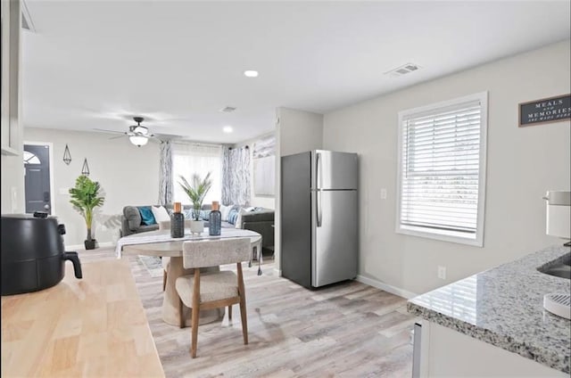 kitchen with stainless steel fridge, white cabinets, ceiling fan, light wood-type flooring, and light stone counters