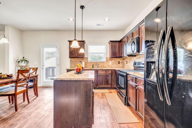 kitchen with pendant lighting, decorative backsplash, a center island, black appliances, and light stone countertops