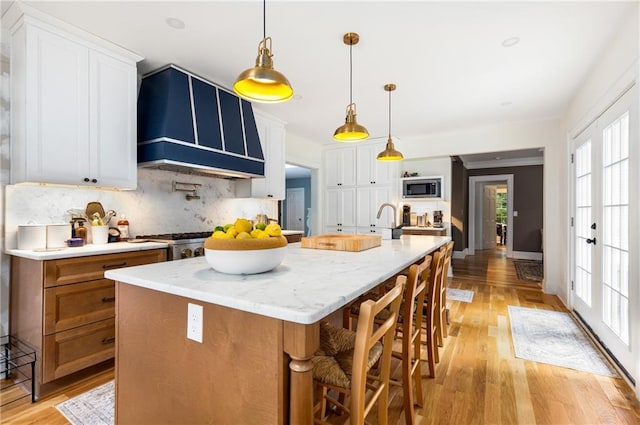 711 Greenview Ave NE, Atlanta, GA 30305 - kitchen featuring backsplash, premium range hood, stainless steel microwave, and light wood-type flooring