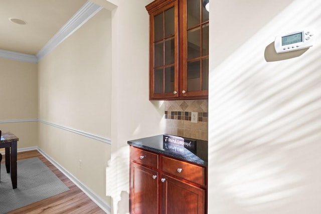 bar featuring decorative backsplash, light wood-type flooring, ornamental molding, and dark stone counters