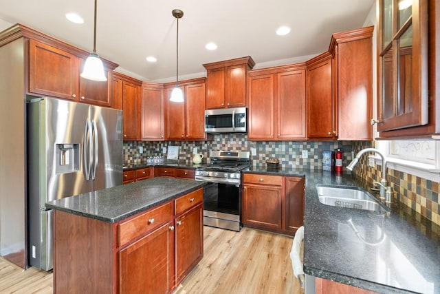 kitchen with appliances with stainless steel finishes, light wood-type flooring, sink, pendant lighting, and dark stone countertops