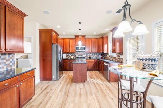 kitchen featuring appliances with stainless steel finishes, tasteful backsplash, pendant lighting, light hardwood / wood-style flooring, and a center island