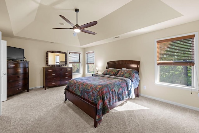 bedroom with a raised ceiling, ceiling fan, and light carpet