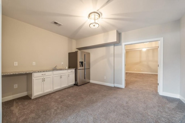 kitchen with sink, light stone counters, stainless steel fridge with ice dispenser, light carpet, and white cabinets