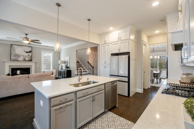 kitchen with appliances with stainless steel finishes, sink, white cabinets, hanging light fixtures, and light stone counters