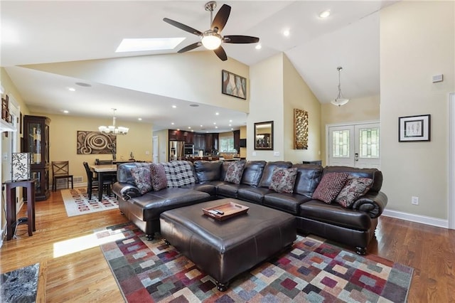 living room featuring dark hardwood / wood-style floors, ceiling fan with notable chandelier, high vaulted ceiling, and a skylight