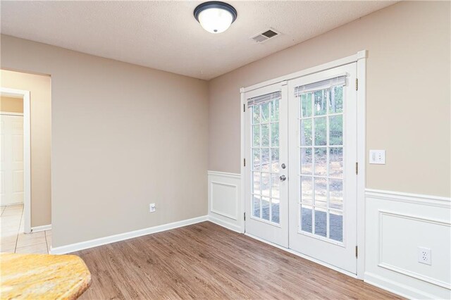 1731 Silverchase SW, Marietta, GA 30008 - spare room featuring light wood-type flooring, french doors, a textured ceiling, a wainscoted wall, and visible vents