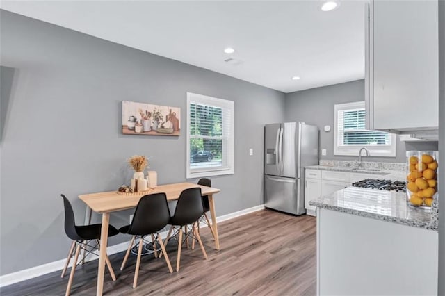 kitchen featuring sink, white cabinetry, appliances with stainless steel finishes, hardwood / wood-style floors, and light stone countertops