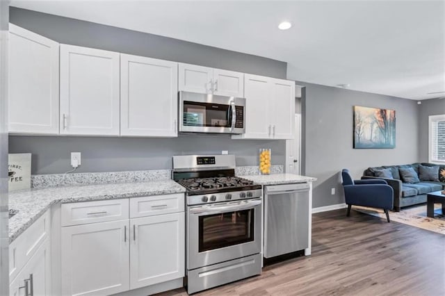 kitchen with light stone countertops, light wood-type flooring, white cabinets, stainless steel appliances, and open floor plan
