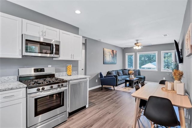 kitchen with light stone counters, a ceiling fan, white cabinets, light wood-style floors, and stainless steel appliances