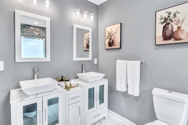 bathroom featuring toilet, double vanity, a sink, and baseboards
