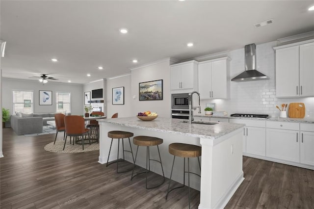 3382 Monarch Ave, Duluth, GA 30096 - kitchen featuring wall chimney range hood, gas cooktop, a kitchen island with sink, crown molding, and white cabinetry
