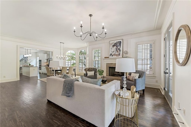 living room featuring dark wood-type flooring, a healthy amount of sunlight, an inviting chandelier, and a brick fireplace