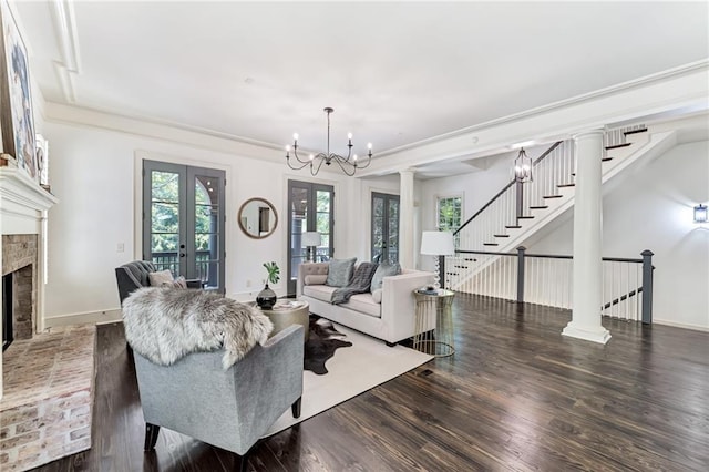 living room featuring hardwood / wood-style floors, french doors, decorative columns, a fireplace, and an inviting chandelier