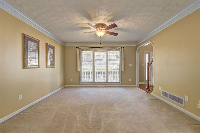 carpeted empty room with baseboards, visible vents, arched walkways, and ornamental molding