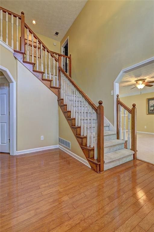 staircase with baseboards, a high ceiling, visible vents, and wood finished floors