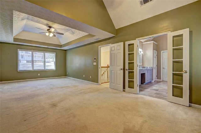 carpeted empty room with baseboards, visible vents, a raised ceiling, ceiling fan, and french doors