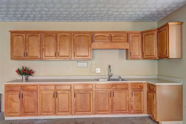 kitchen featuring a textured ceiling, brown cabinets, a sink, and light countertops