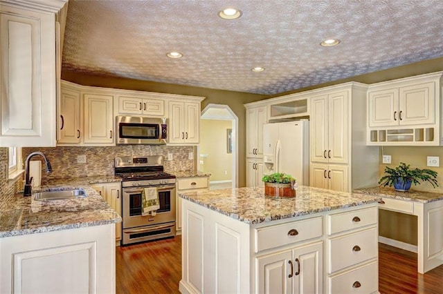 kitchen featuring dark wood-style floors, light stone counters, stainless steel appliances, open shelves, and a sink