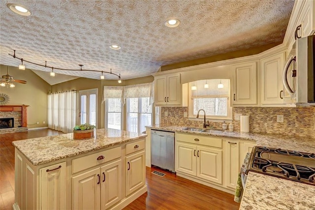 kitchen with appliances with stainless steel finishes, wood finished floors, vaulted ceiling, a stone fireplace, and a sink