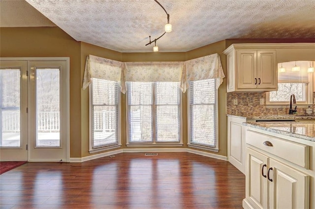 kitchen featuring tasteful backsplash, baseboards, dark wood-style floors, light stone countertops, and a textured ceiling