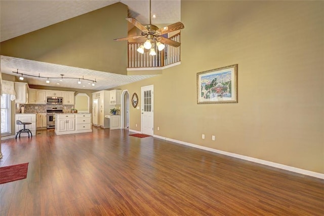 unfurnished living room with arched walkways, a high ceiling, dark wood-type flooring, a ceiling fan, and baseboards