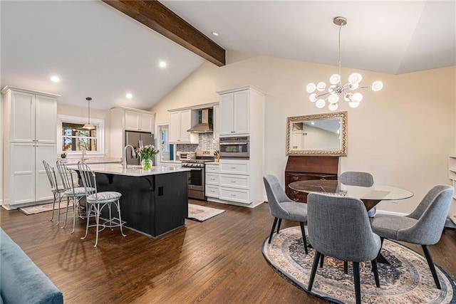 kitchen with dark wood-style floors, appliances with stainless steel finishes, a kitchen breakfast bar, vaulted ceiling with beams, and wall chimney range hood