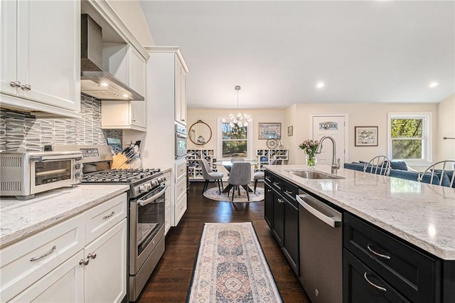 kitchen featuring appliances with stainless steel finishes, dark cabinetry, a sink, and wall chimney exhaust hood