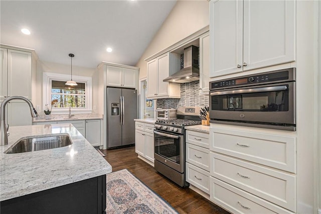 kitchen featuring appliances with stainless steel finishes, a sink, wall chimney range hood, pendant lighting, and backsplash