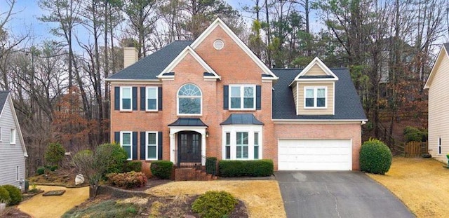 colonial home with brick siding, a chimney, and aphalt driveway