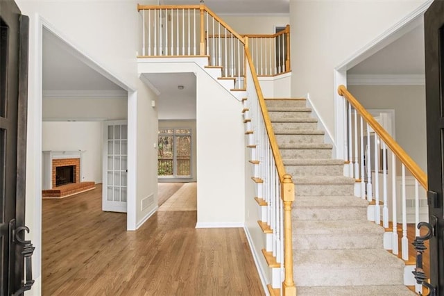 stairway featuring crown molding, a fireplace, baseboards, and wood finished floors