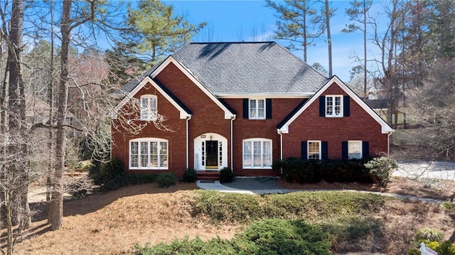 colonial-style house featuring brick siding and roof with shingles