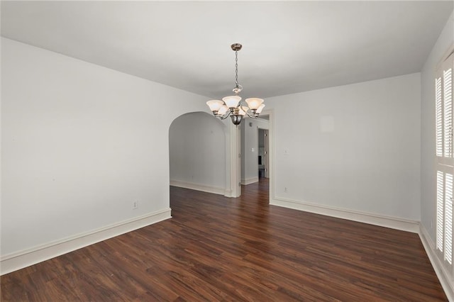 spare room featuring baseboards, arched walkways, a notable chandelier, and dark wood-style floors