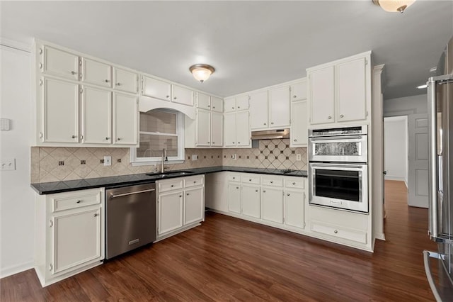 kitchen featuring dark wood finished floors, a sink, stainless steel appliances, under cabinet range hood, and dark countertops