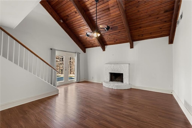 unfurnished living room with wood finished floors, high vaulted ceiling, beam ceiling, a fireplace with raised hearth, and stairs