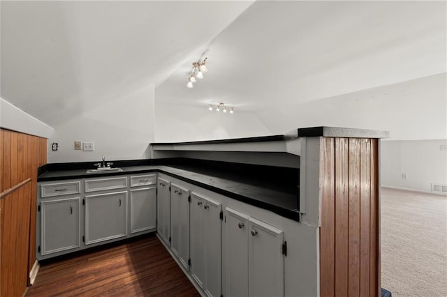 kitchen featuring gray cabinets, a sink, dark countertops, dark colored carpet, and vaulted ceiling