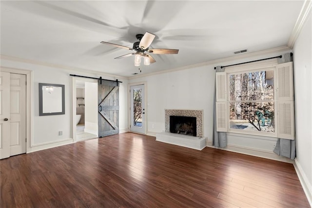 unfurnished living room with visible vents, ornamental molding, wood finished floors, a barn door, and ceiling fan