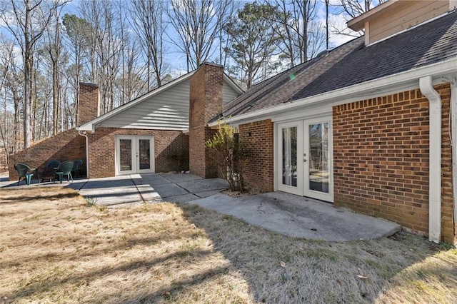 back of house featuring french doors, roof with shingles, brick siding, a chimney, and a patio area