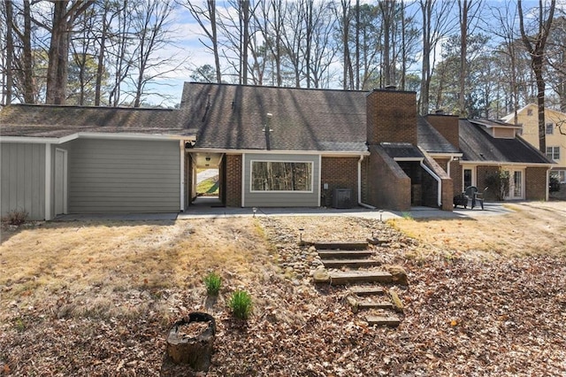 rear view of house with a patio area, brick siding, and a chimney