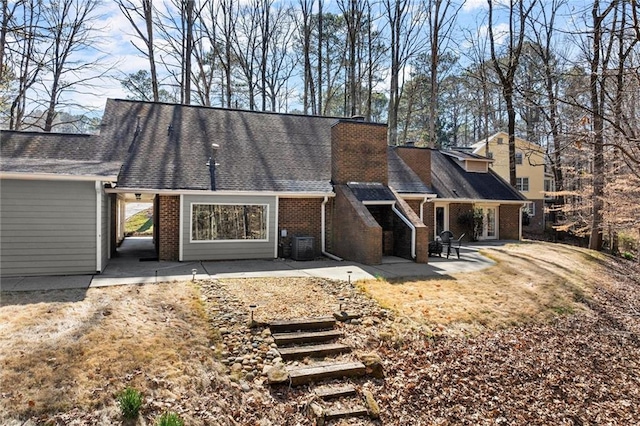 rear view of property with brick siding, a chimney, and a patio area