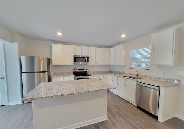 kitchen with white cabinetry, light stone counters, a center island, light wood-type flooring, and stainless steel appliances