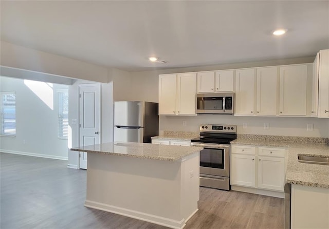 kitchen featuring light stone countertops, stainless steel appliances, a center island, and white cabinets