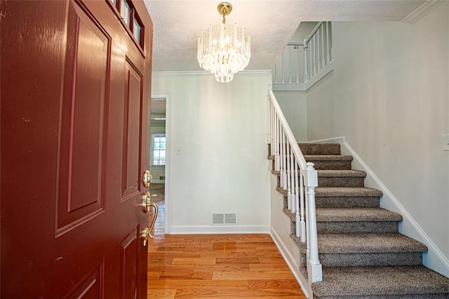 foyer entrance featuring ornamental molding, an inviting chandelier, and light hardwood / wood-style flooring