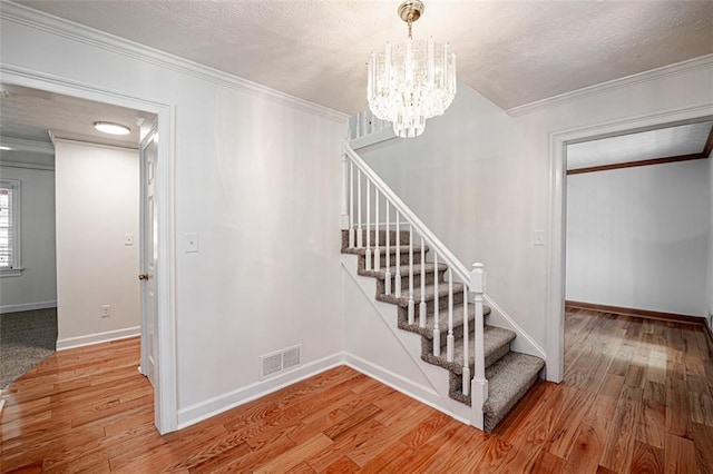 stairs with a notable chandelier, crown molding, a textured ceiling, and hardwood / wood-style flooring