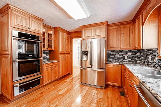 kitchen with a textured ceiling, light hardwood / wood-style floors, sink, appliances with stainless steel finishes, and light stone countertops