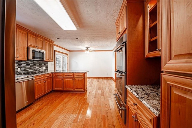 kitchen featuring appliances with stainless steel finishes, stone countertops, light wood-type flooring, crown molding, and ceiling fan