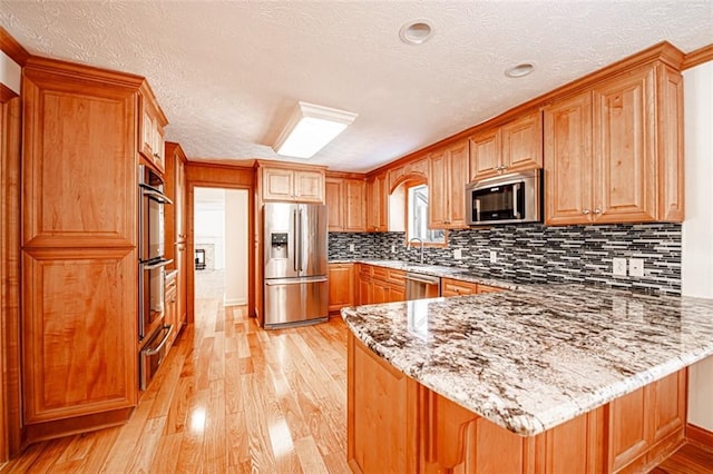 kitchen featuring light stone counters, stainless steel appliances, light wood-type flooring, and kitchen peninsula