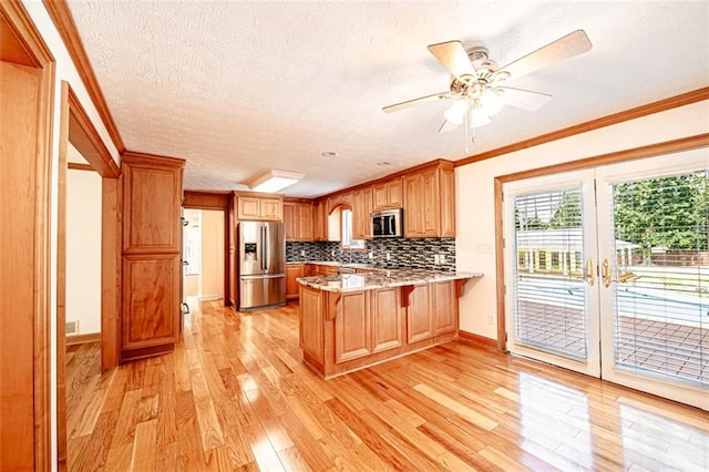 kitchen featuring ceiling fan, ornamental molding, kitchen peninsula, appliances with stainless steel finishes, and light wood-type flooring